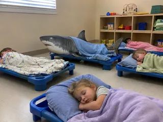 Children napping at daycare alongside a toy shark.